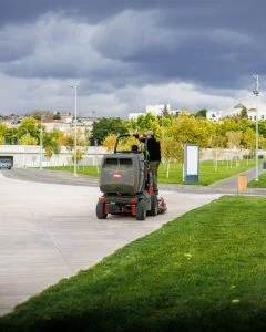 A park employee driving a lawnmower on a cloudy day in an urban park setting.